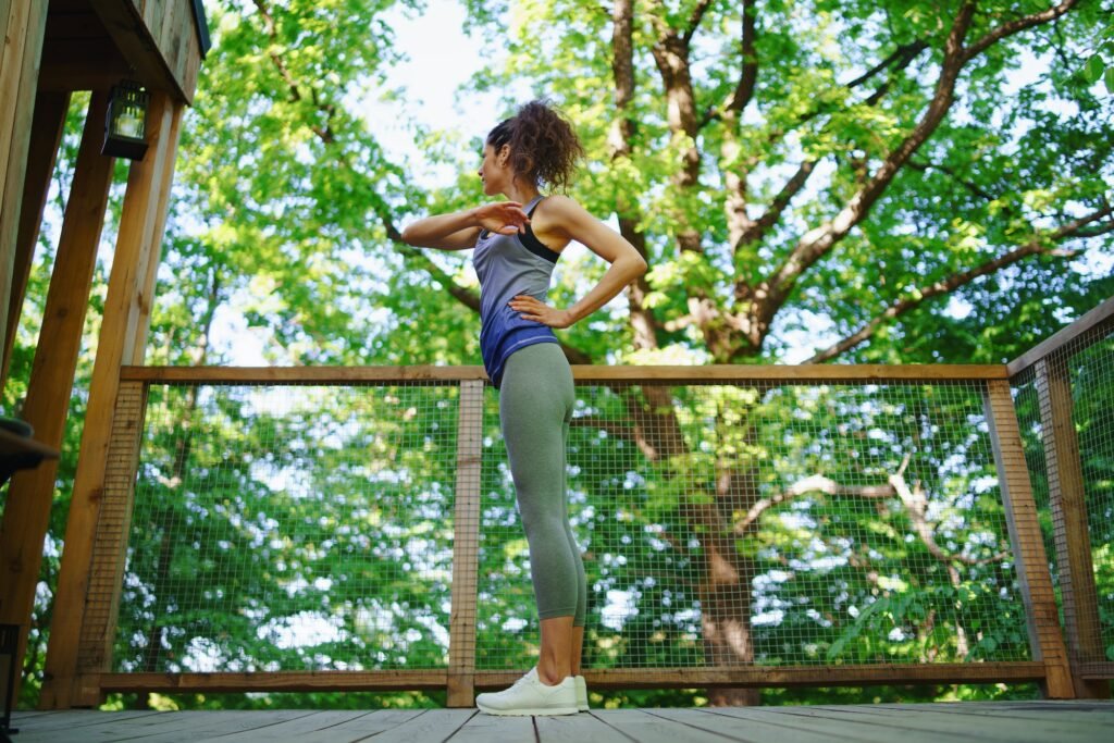 Woman doing exercise outdoors on terrace of tree house, weekend away and digital detox concept.