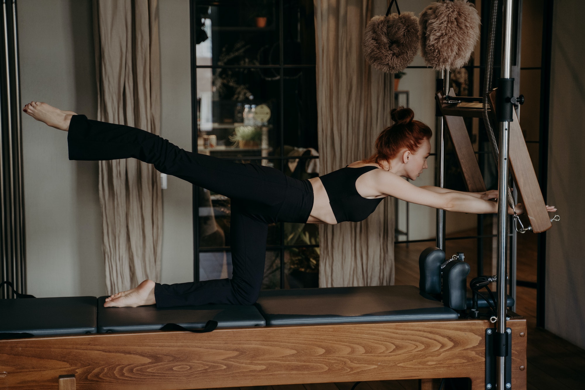 Young ginger athletic woman exercising on pilates reformer in studio