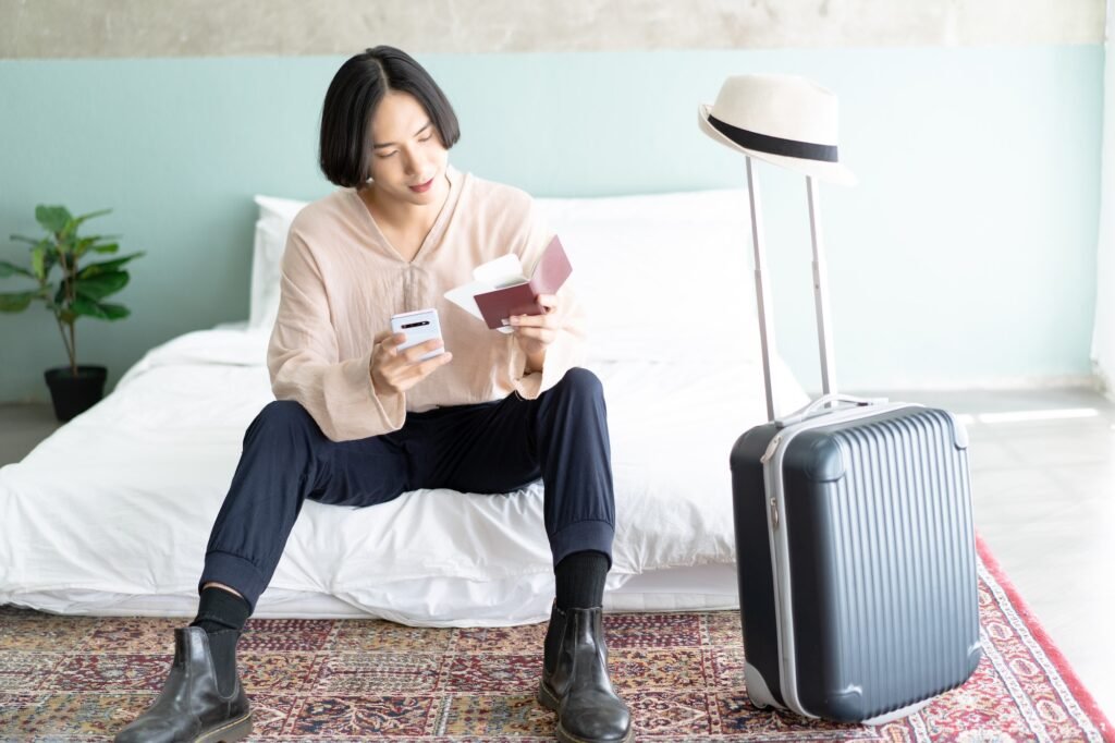 Asian man sit on bed in hotel room accomodation while checking his flight online for holiday