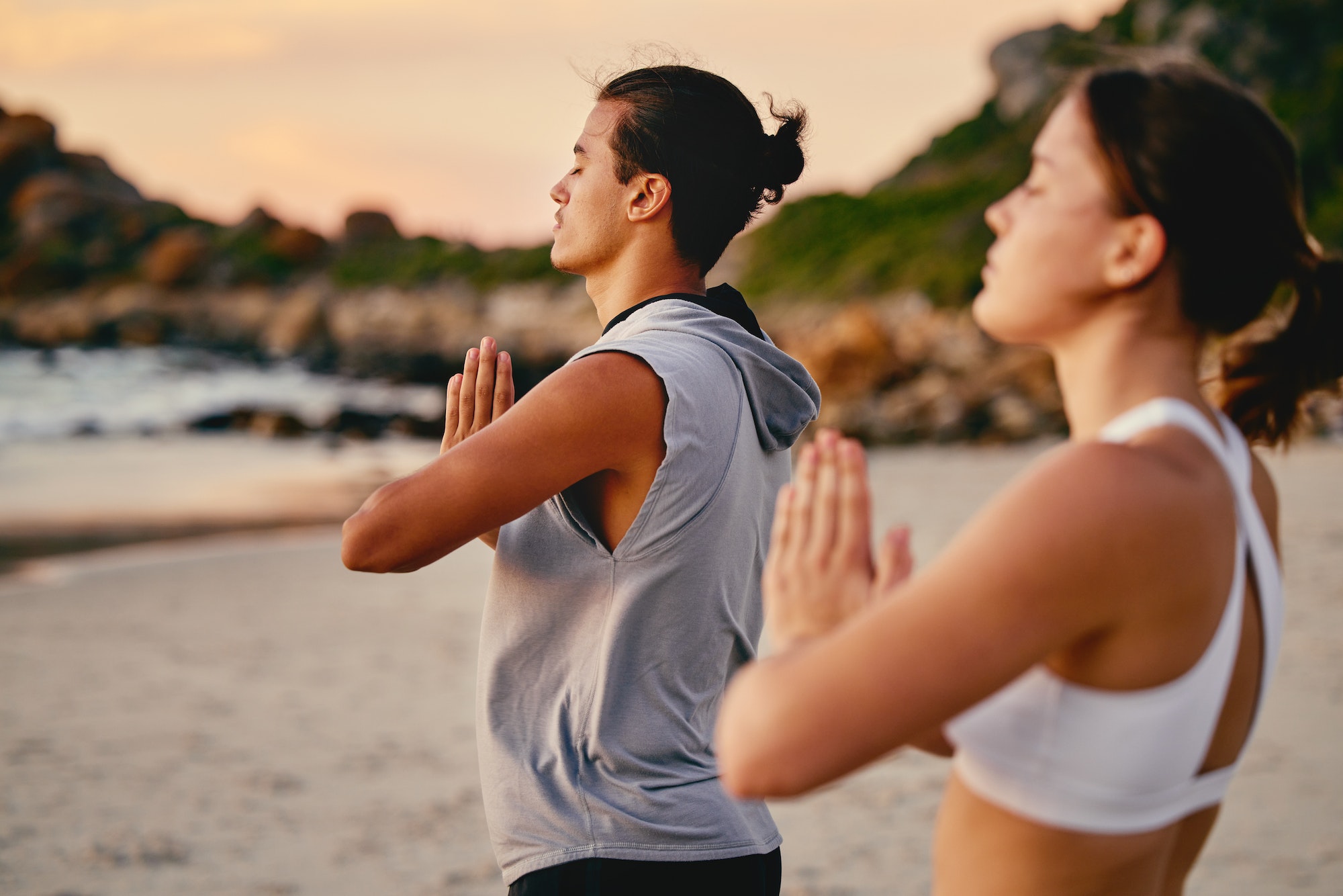 Couple, prayer hands and yoga meditation at beach outdoors for health and wellness. Sunset, pilates,