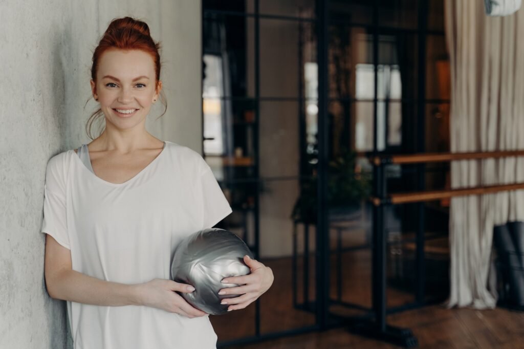 Happy active ginger woman with mini fitball relaxing after workout in fitness studio