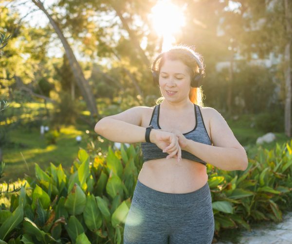 Fat woman checking time or heart rate from smart watch. Exercise or running outdoors for weight loss