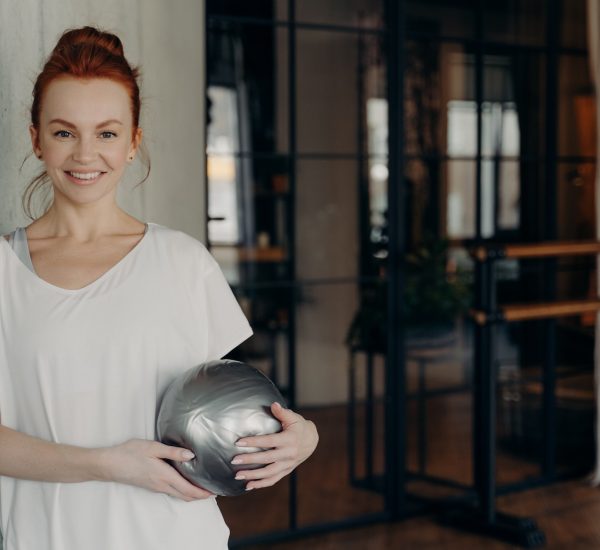 Happy active ginger woman with mini fitball relaxing after workout in fitness studio