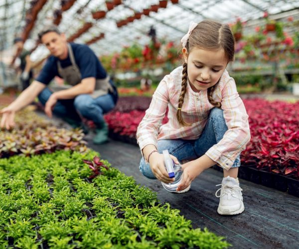 Little girl using spray bottle and nourishing plants in a greenhouse, Eco-Friendly Wellness Retreats