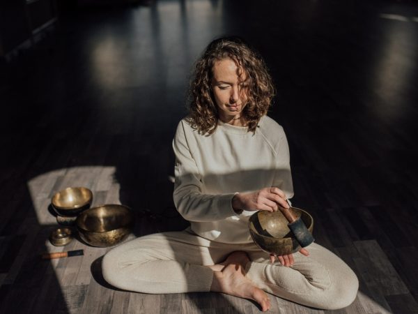 Spiritual practitioner playing bowl gong on floor in sunlight