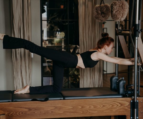 Young ginger athletic woman exercising on pilates reformer in studio